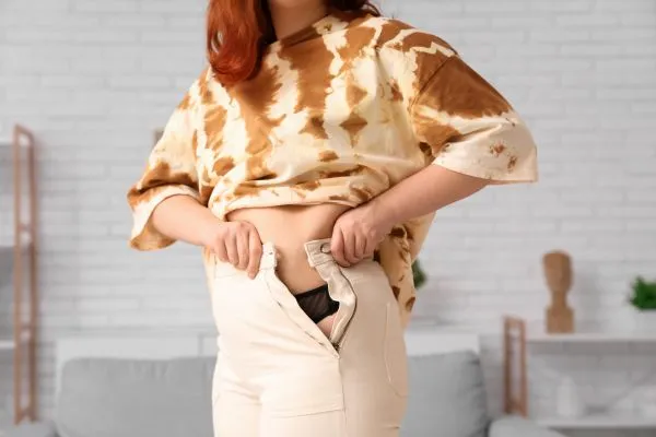 Image of woman trying to do her trousers up after pregnancy weight gain Ascot